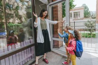 Two student enter shcoll while teacher holds open the door